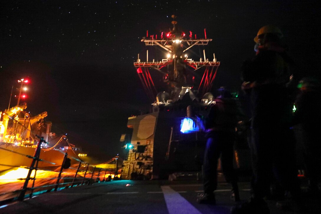 Two ships sail next to each other at night illuminated by red and blue lights.