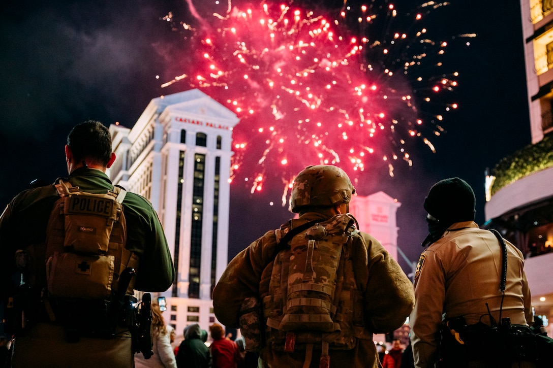 A solider and two police officers watch a fireworks show.