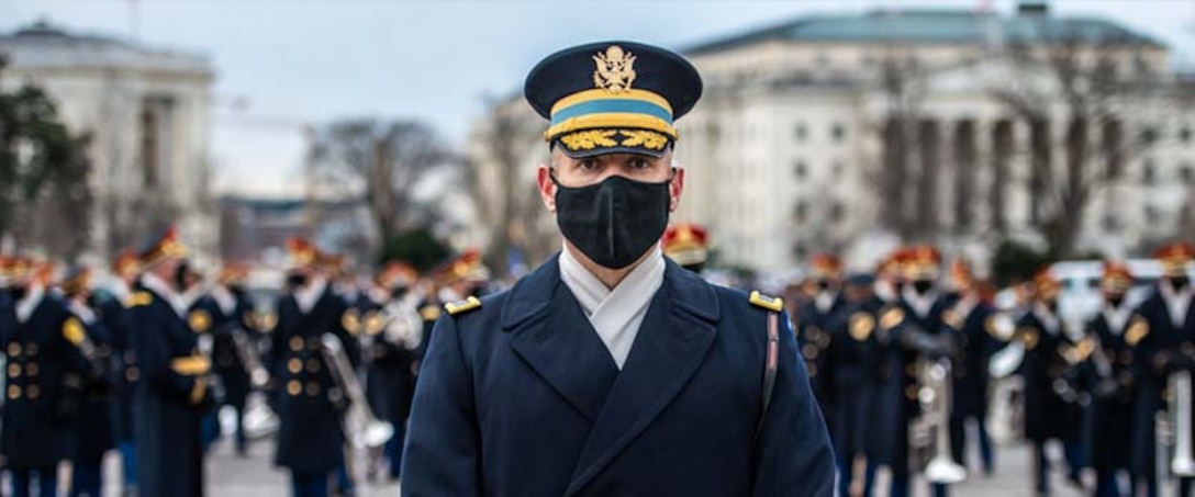 A soldier of the Army's Old Guard stands in the foreground of other soldiers all in service dress.