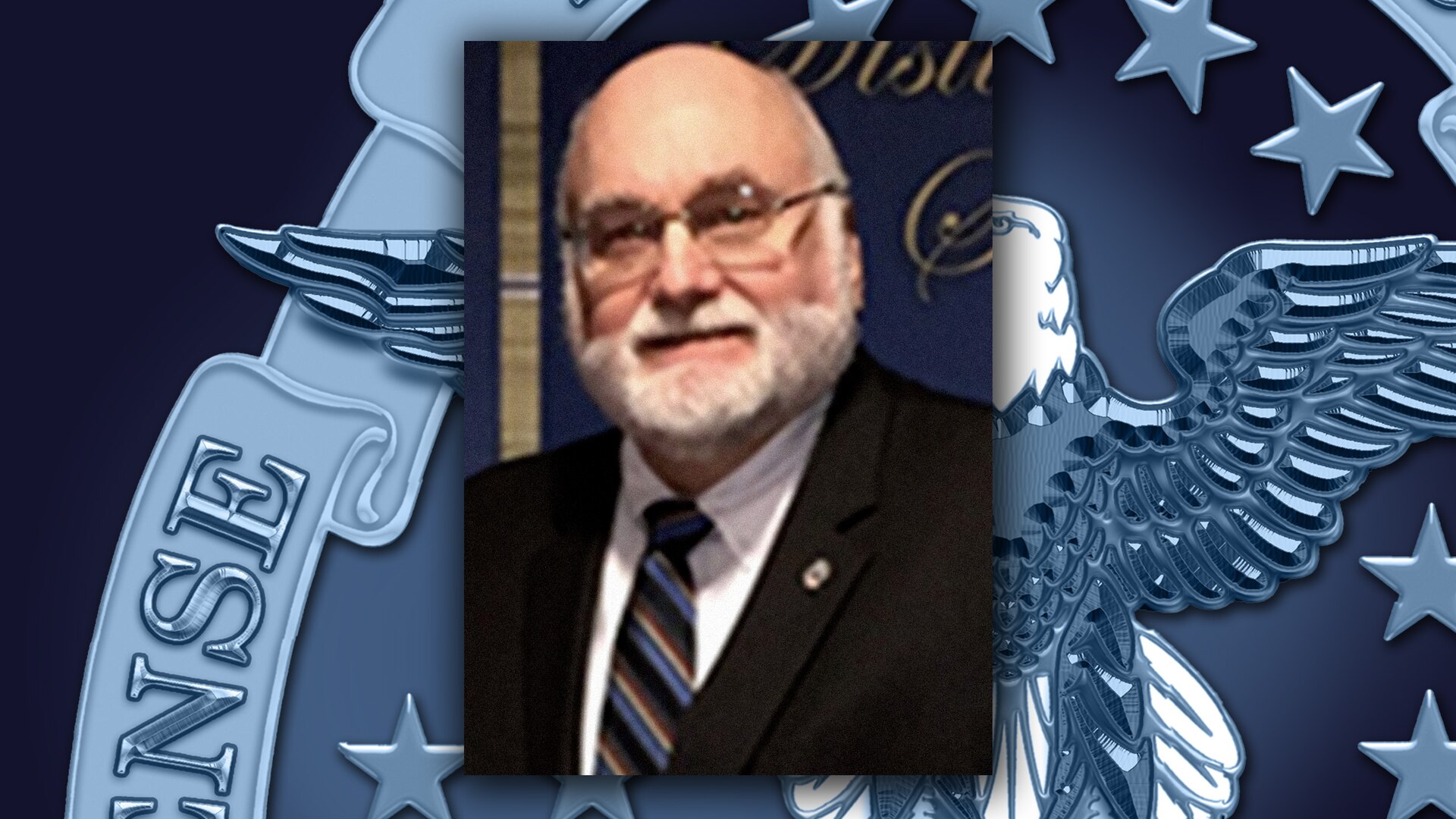 Head and shoulders shot of a white man with a beard and eyeglasses wearing a dark suit.