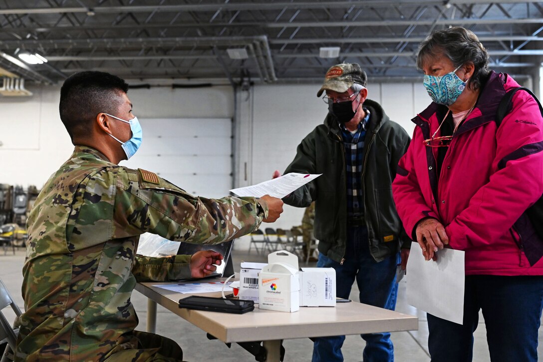 A soldier wearing a face mask hands paperwork to a man and woman.