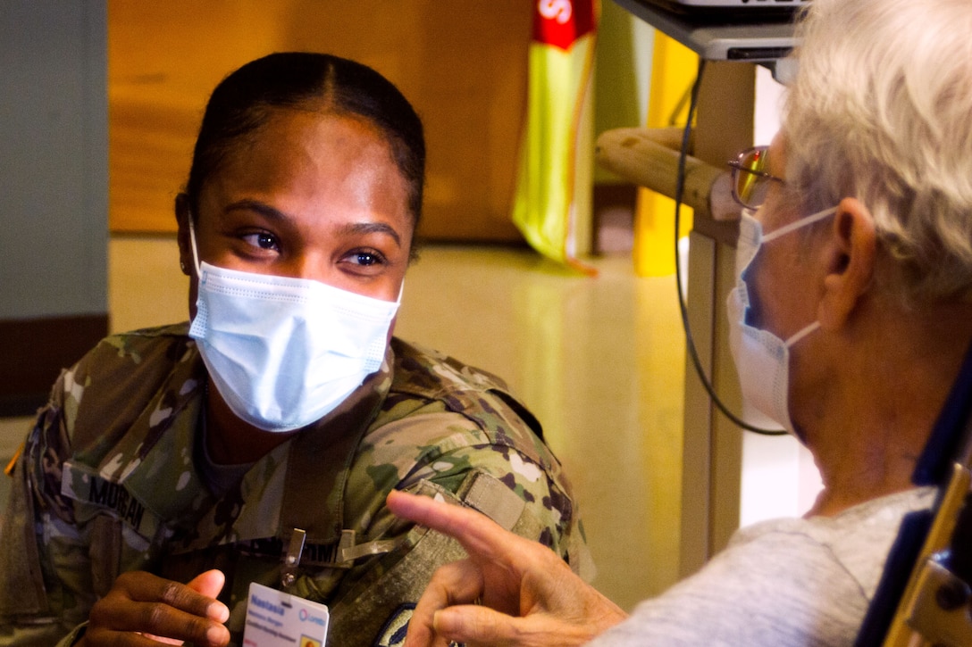 A soldier wearing a face mask smiles at a resident.