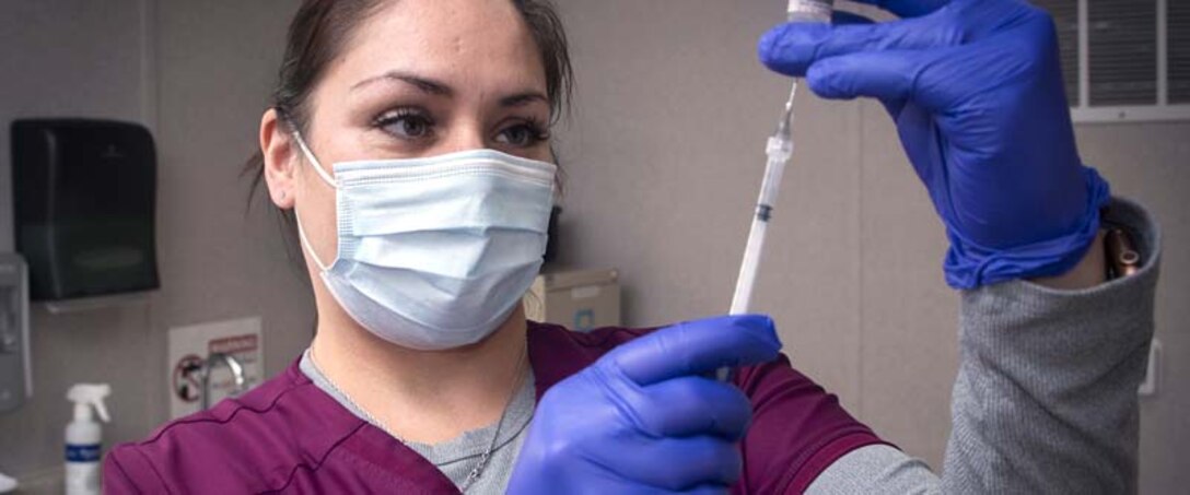 Female in nurse scrubs and a face mask and gloves prepares a needle.