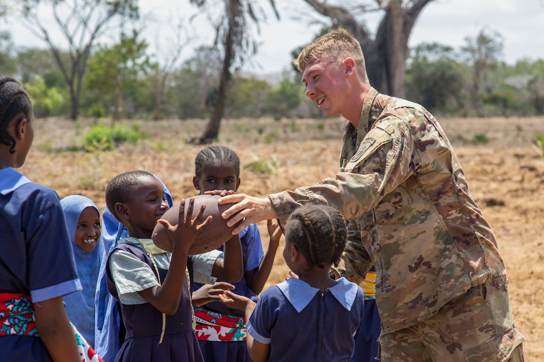 U.S. Army Spc. David Fox with C Company, 1-102nd Infantry Regiment (Mountain), Task Force Iron Gray, Combined Joint Task Force – Horn of Africa (CJTF-HOA), plays with a football with students during a cultural engagement at a school in Lamu County, Kenya, Nov. 2, 2021. CJTF-HOA efforts, as part of a comprehensive whole-of-government approach, are aimed at increasing African partner nations’ capacity to maintain a stable environment, with an effective government that provides a degree of economic and social advancement to its citizens.
