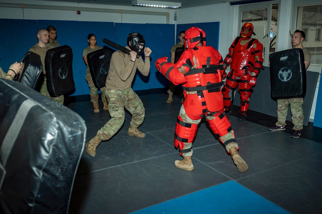 An airman wearing safety gear fights an instructor wearing a red combat suit during training.