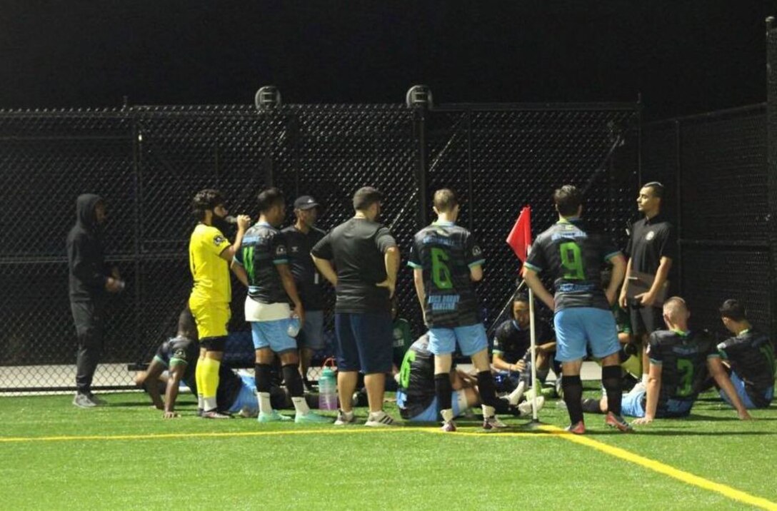 Soccer players talk on the sideline of a field.