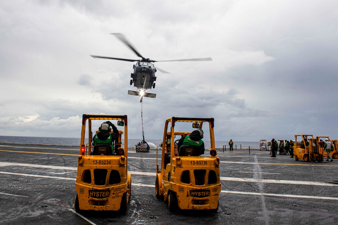 A helicopter drops supplies on an aircraft carrier.