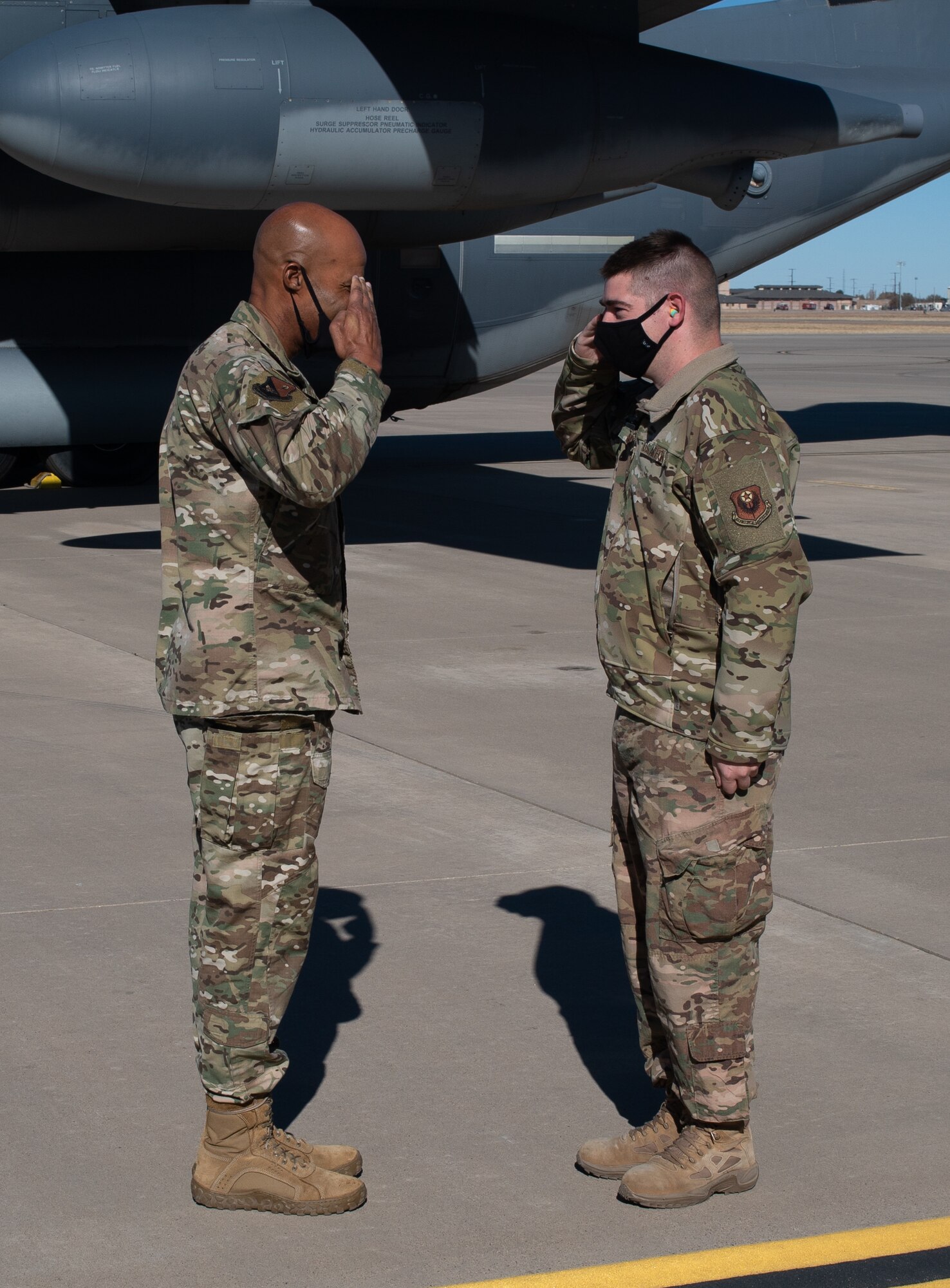 An Air Force Colonel salutes an Airman in front of a military cargo aircraft.