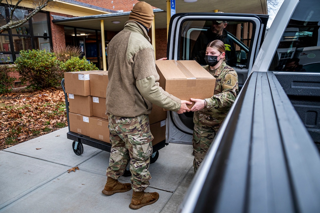 Two soldiers wearing face masks carry a box into a truck.