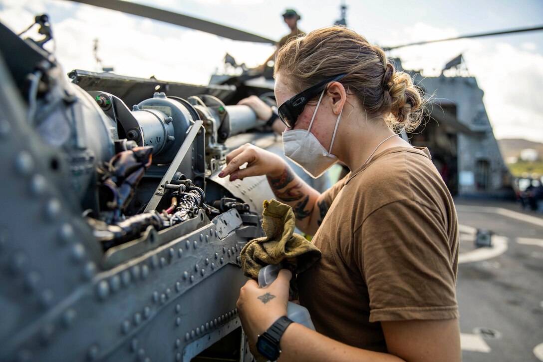 A sailor cleans the transmission of a helicopter aboard a ship.