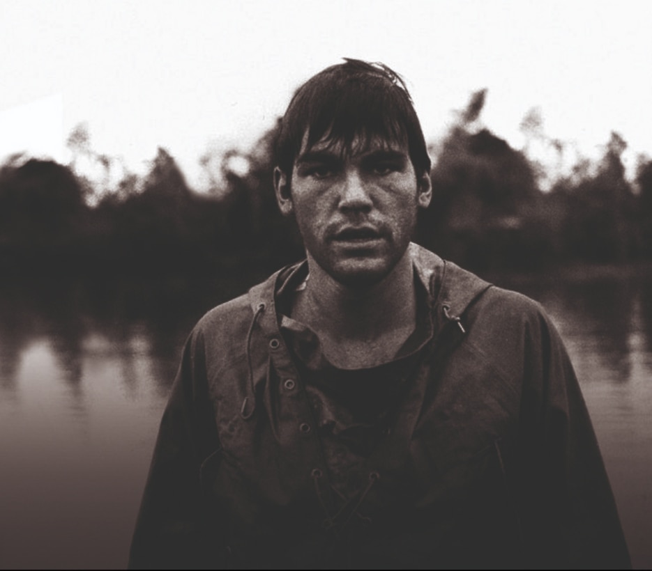 A man poses for a photo in front of a body of water.