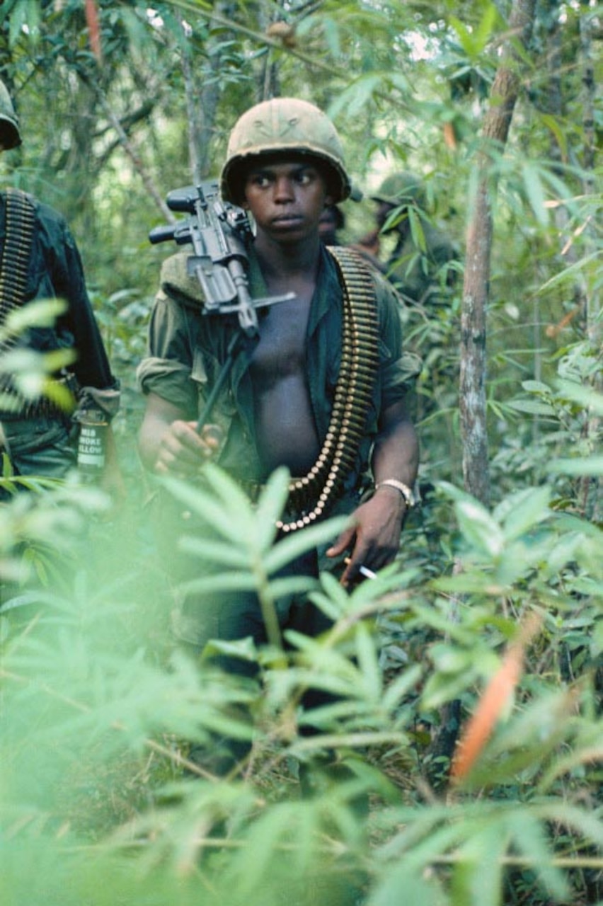 Soldiers walk through a jungle.