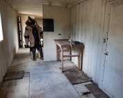 An EOD tech, wearing a bomb suit, peers into a room at an IED device during an IED training scenario.