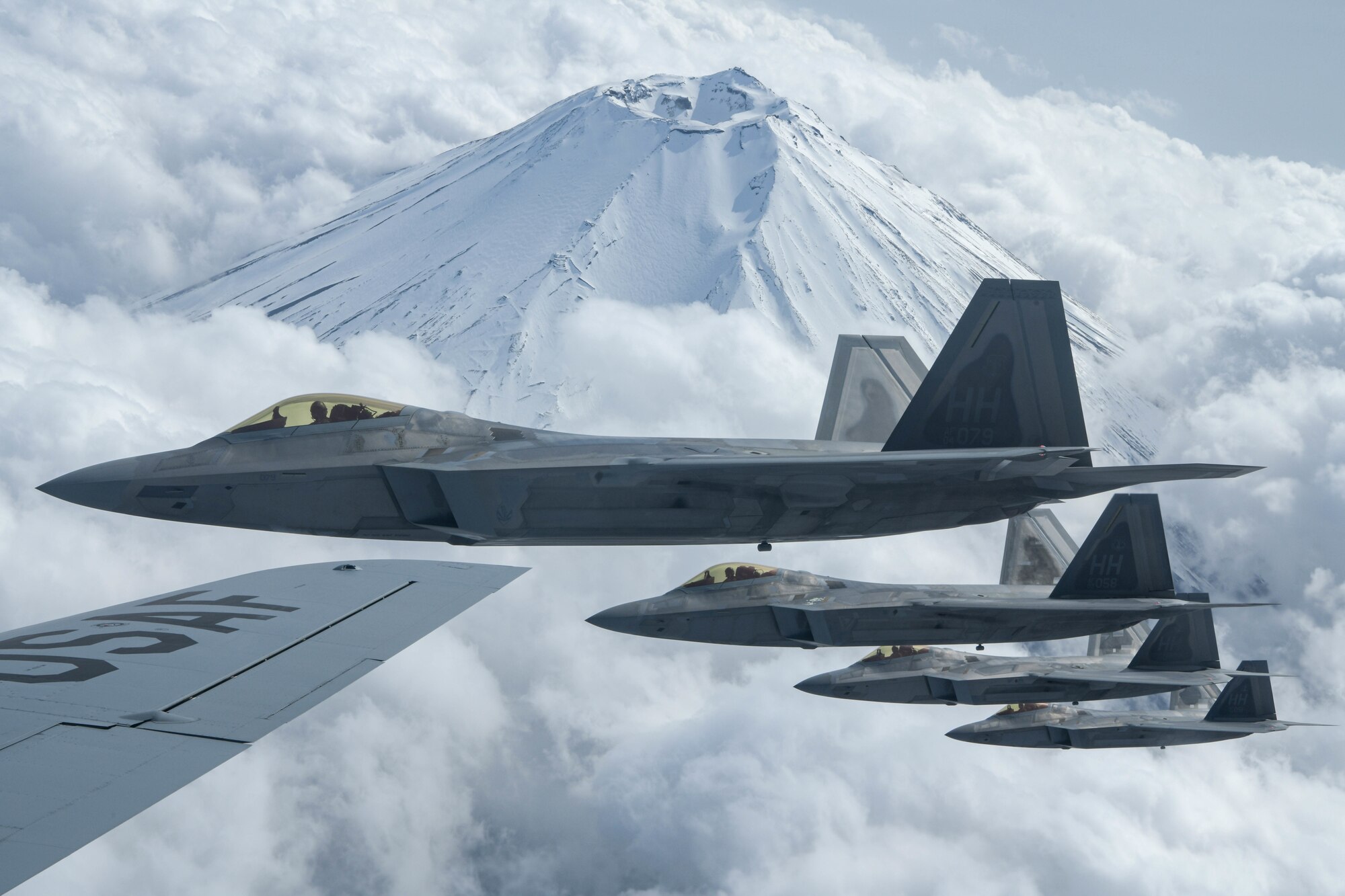 Four F-22 Raptors from the 199th Fighter Squadron fly alongside a U.S. Air Force KC-135 Stratotanker