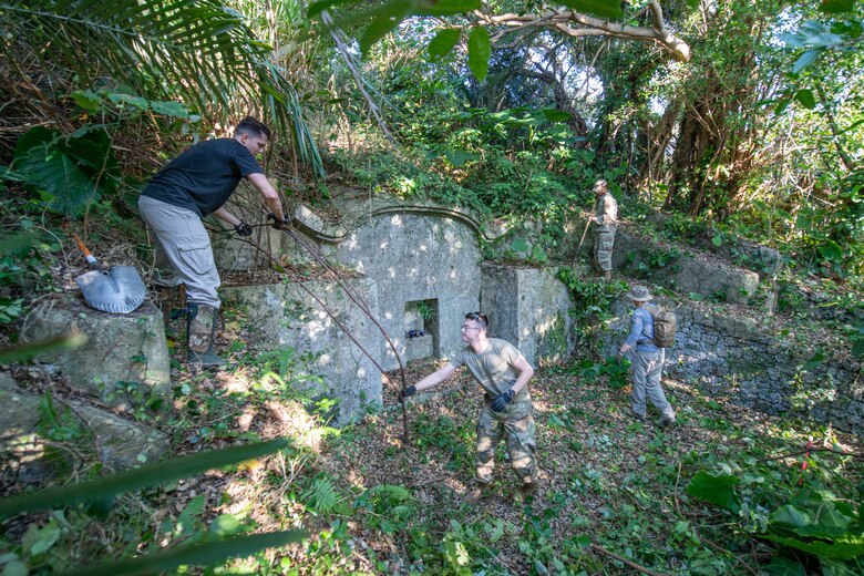 Airmen work together to clear branches, leaves and overgrown vegetation at a shrine