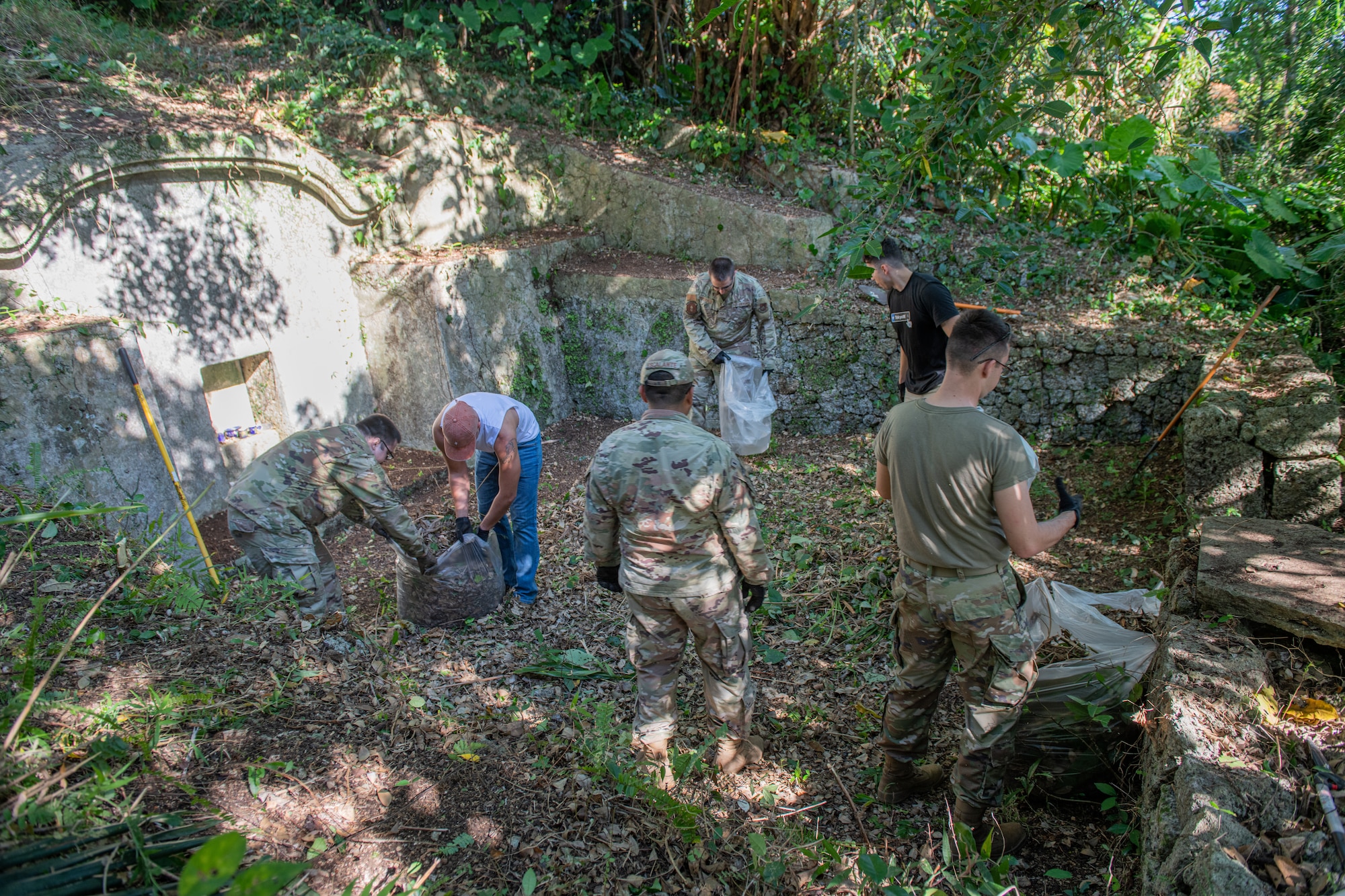 Airmen put shrubbery they cleared from a shrine in bags