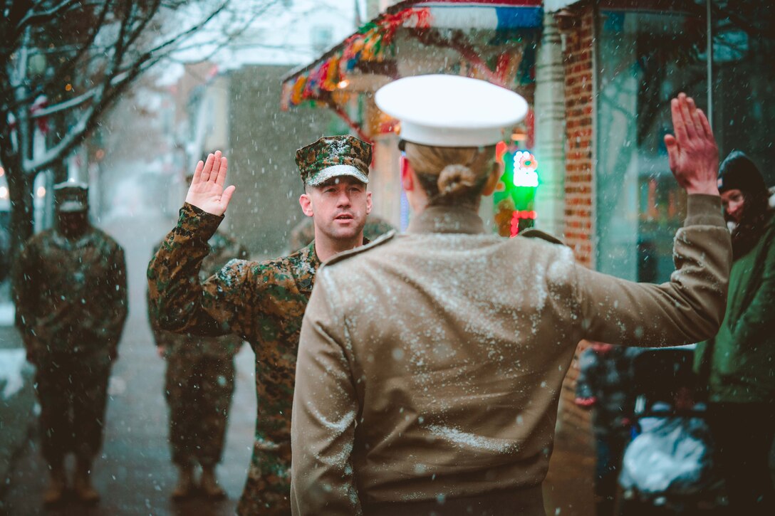 Two people stand face to face holding their right hands up in the snow.