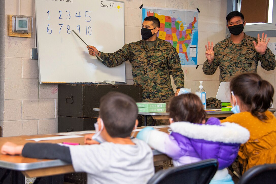 Two Marines wearing face masks instruct Afghan children evacuees in a classroom.