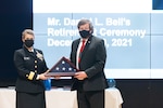 Woman in black US Navy uniform hands a folded US Flag in a box to a man in a black suit on a stage.