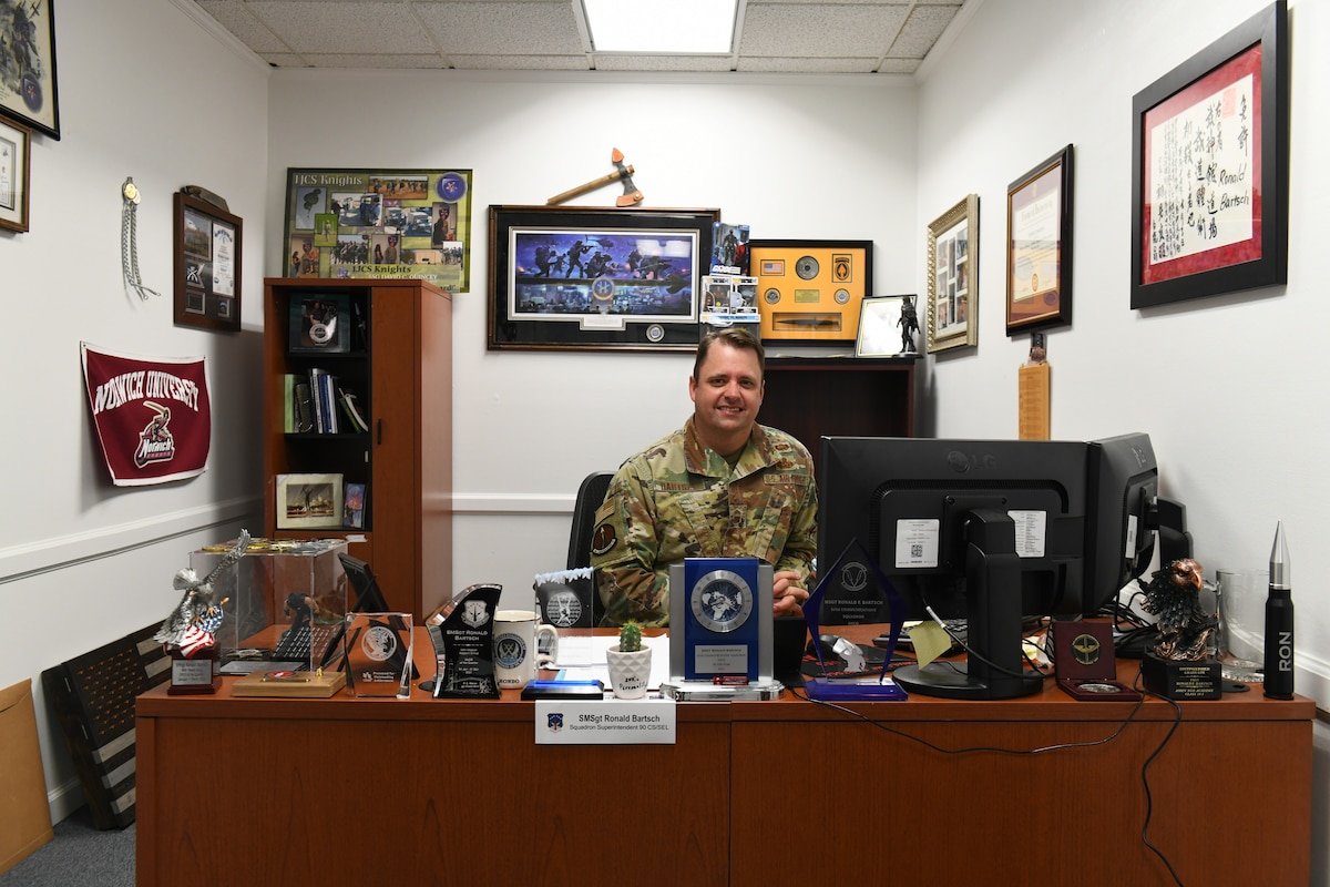 Senior Bartsch poses at his desk, decorations and mementos surrounding him