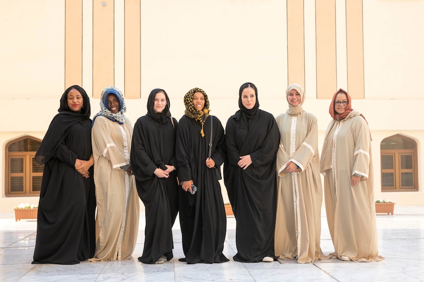 Seven women wearing hijabs stand in a row outside a building.
