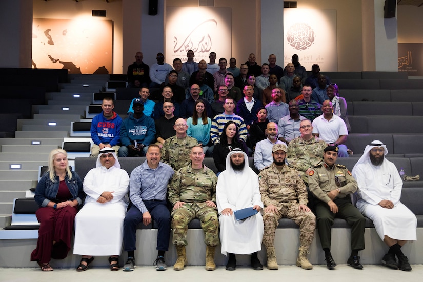 Soldiers and civilians sit on bleachers for a group photo.