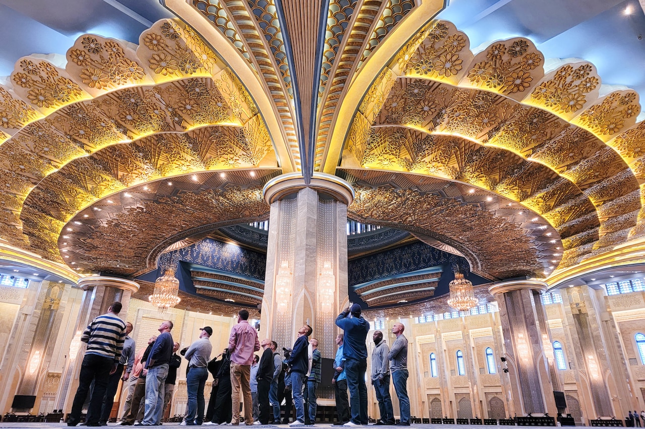 People look up at an ornate ceiling in a big room.