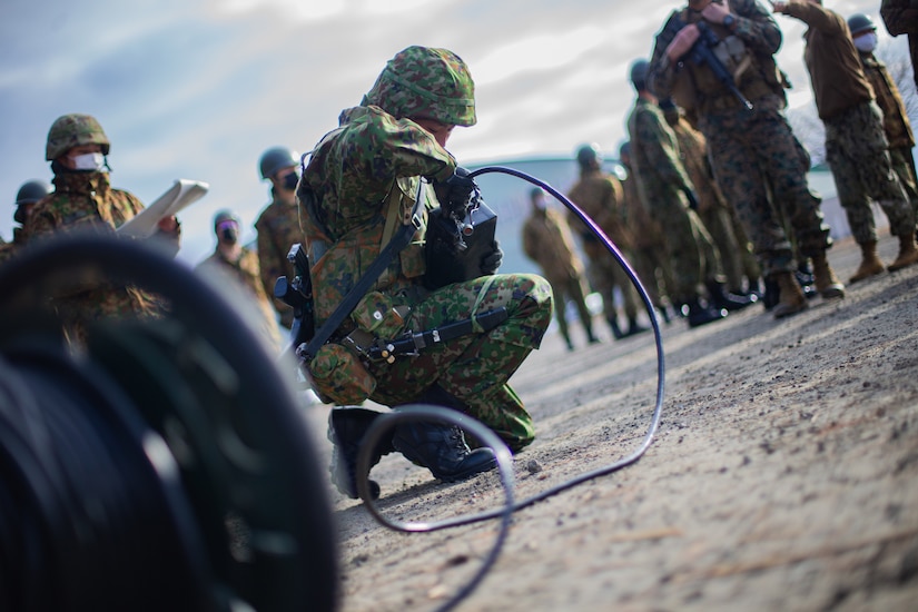A soldier kneels on the ground while handling equipment.