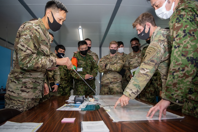 Military members stand around a map table.