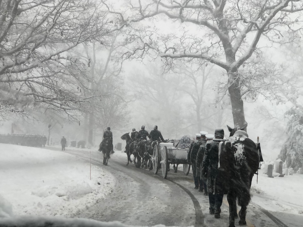 Marines travel through snow, some on horseback and others walking behind a carriage.