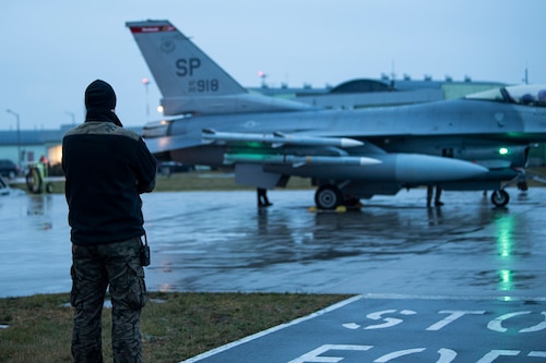 A Polish Air Force member watches an F-16 Fighting Falcon assigned to the 480th Fighter Squadron at Spangdahlem Air Base, Germany, arrive at Łask Air Base, Poland, January 4, 2022.