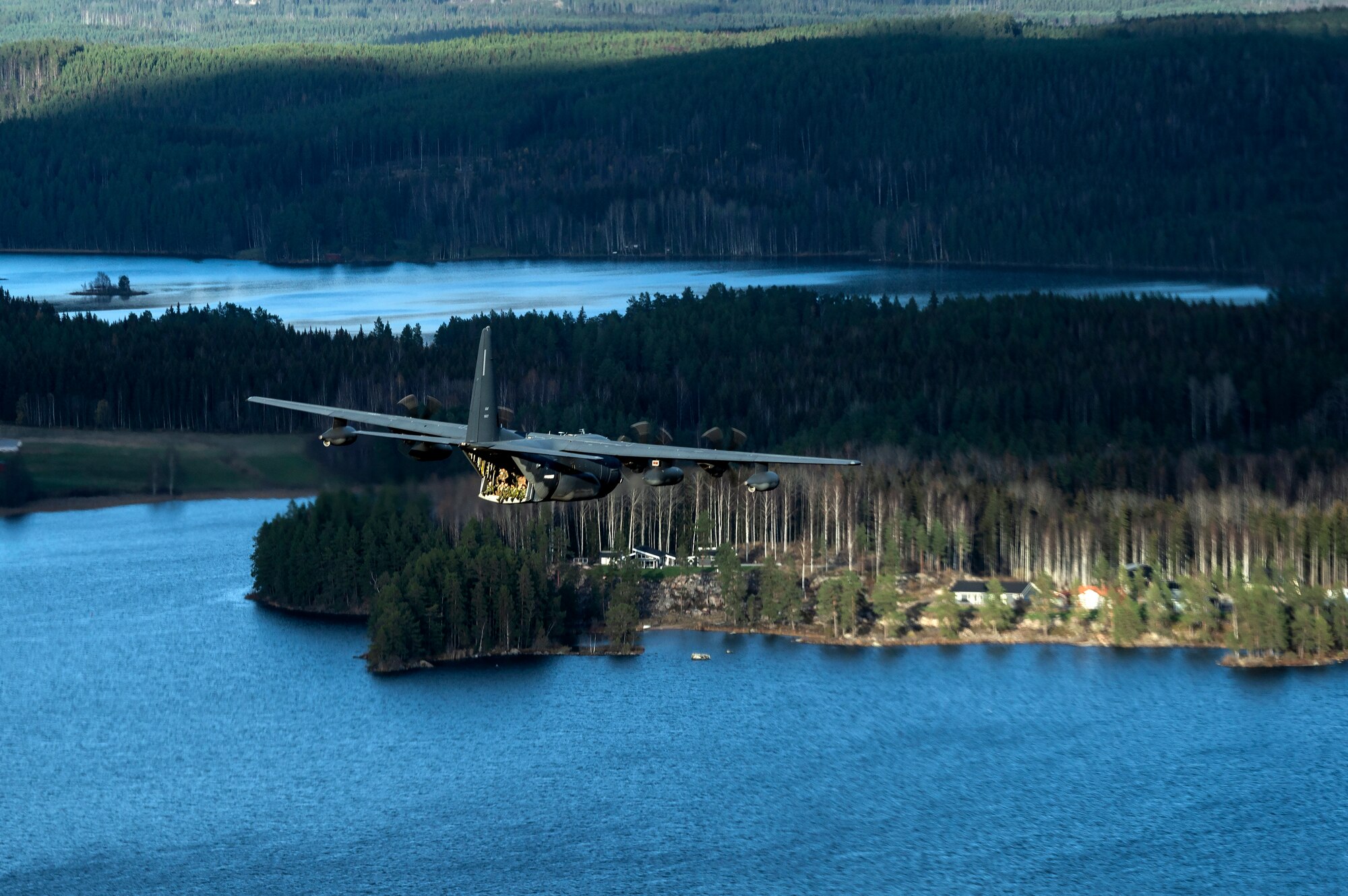 U.S. Air Force and Swedish Air Force members sit on the tail of an MC-130J Commando II assigned to the 352d Special Operations Wing, during a low level formation flight