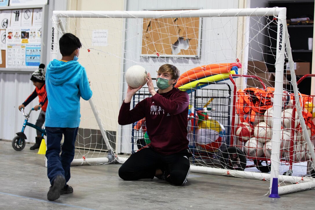 A volunteer wearing a face mask tosses a ball to an Afghan evacuee during a soccer game.