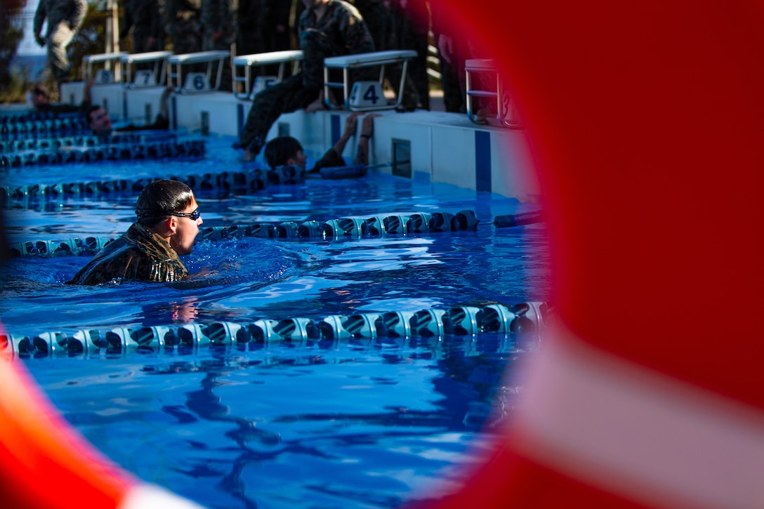 A Marine swims in a pool as seen through the hole in a life preserver.