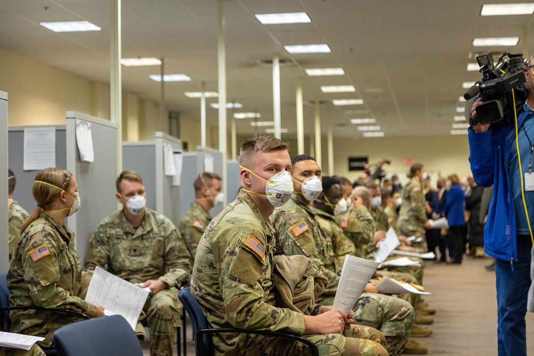 Members of the Guard in OCP uniforms sit in the National Guard Center waiting to be in-processed for deployment.