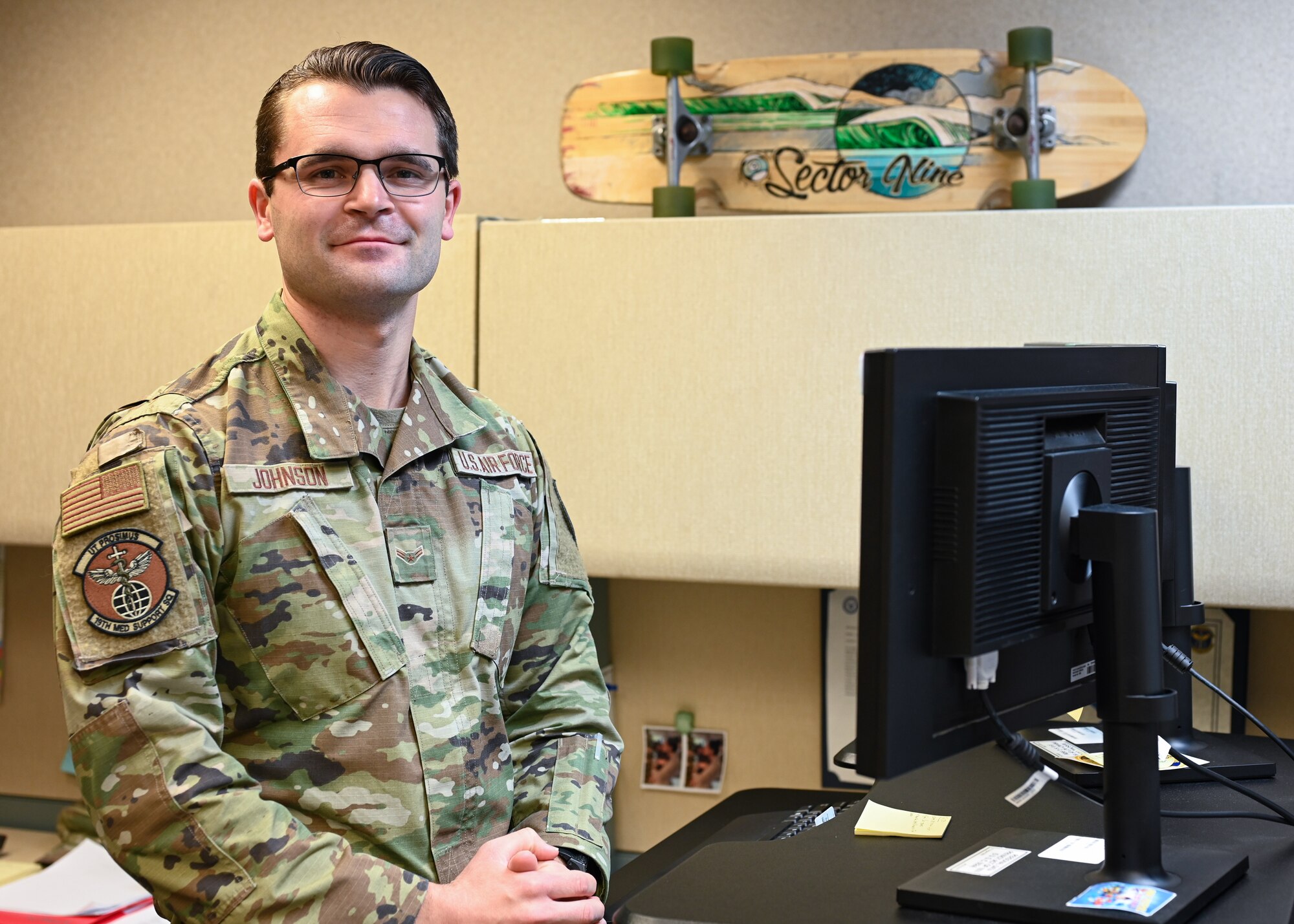 An Airman stands in front of his desk