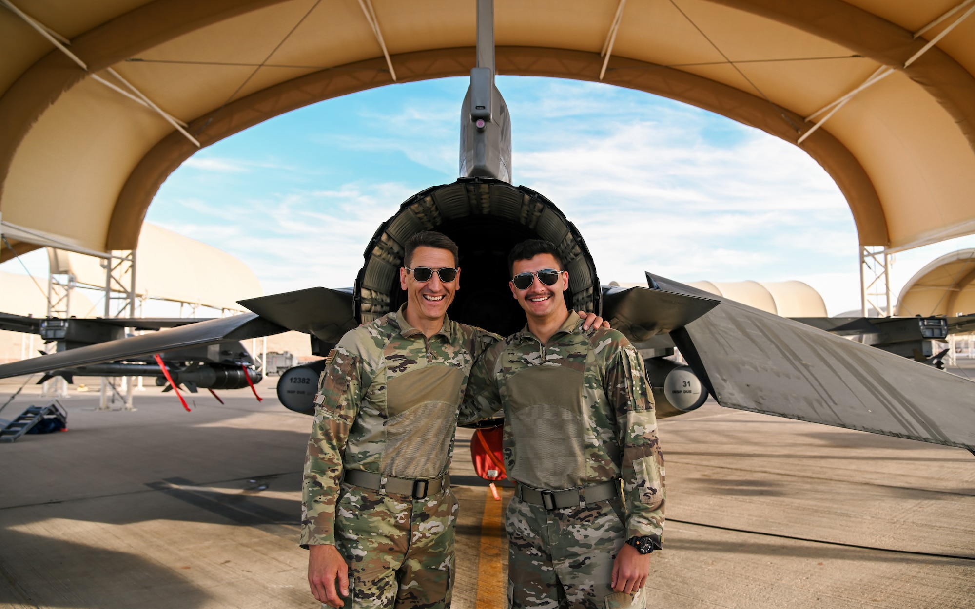 Senior Master Sgt. Steve Veers, 176th Expeditionary Fighter Squadron aerospace propulsion superintendent, and Airman 1st Class Isac Veers 176th EFS aviation resource management journeyman, pose for a photo in front of an F-16 Fighting Falcon at Prince Sultan Air Base, Kingdom of Saudi Arabia, Dec. 13, 2021. The father and son duo deployed to the 378th Air Expeditionary Wing together from the 115th Fighter Wing, Madison, Wisconsin. (U.S. Air Force photo by Staff Sgt. Christina Graves)