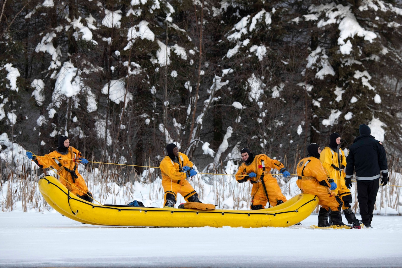 A group of airmen tug a line with an inflatable craft on the snow and ice.