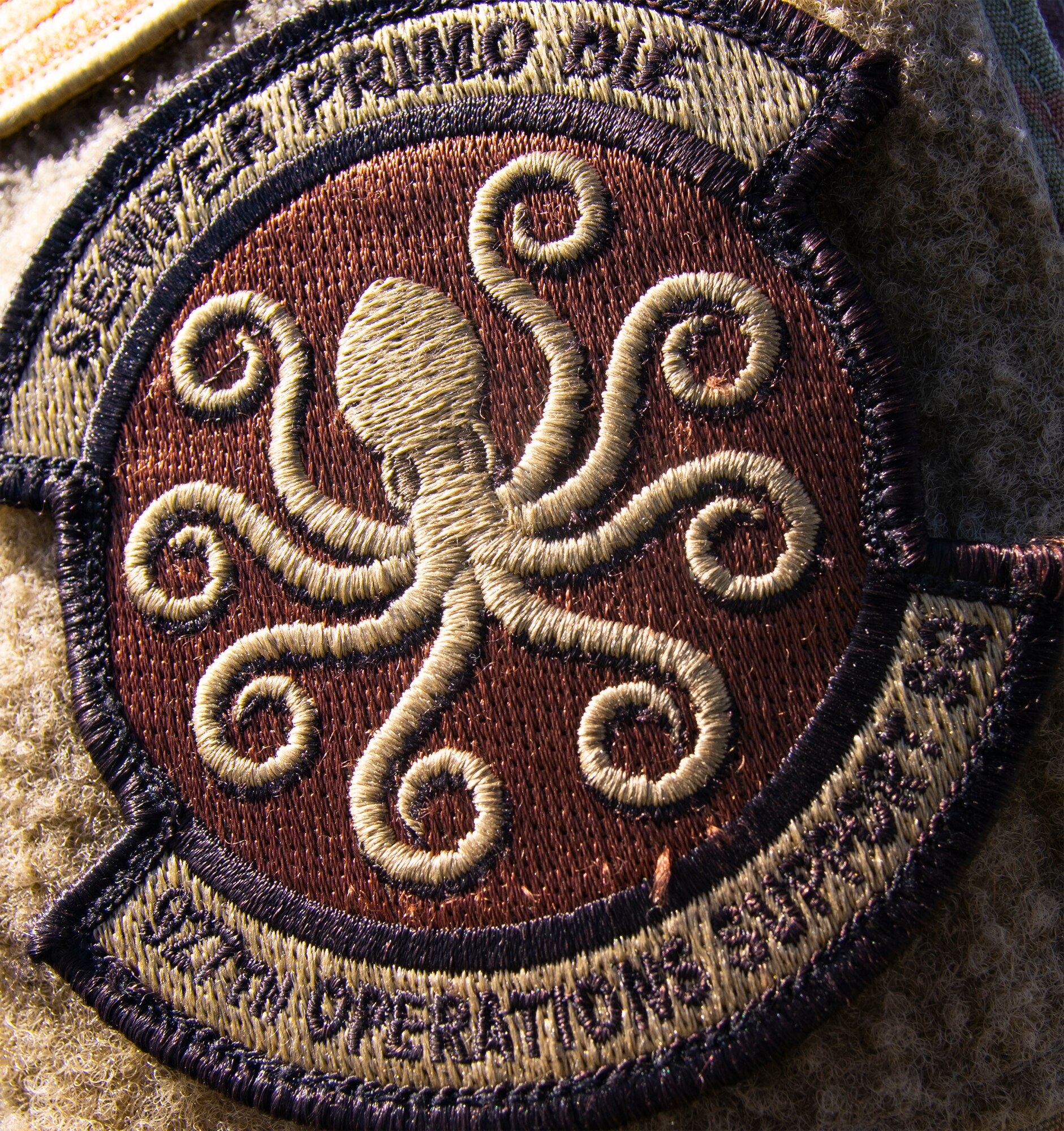 The newly approved emblem of the 927th Operations Support Squadron is pictured in the configuration and color scheme for the Air Force Occupational Camouflage Pattern uniform. Illustrated within the patch is an eight-armed sea monster known as the kraken, as well as the Squadron’s motto “Semper Primo Die,” which is Latin for “Always the first day.” (U.S. Air Force photo by Tech Sgt. Bradley Tipton)