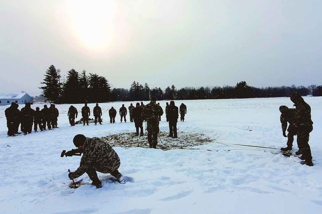 Soldiers build a tent in a snowy field.