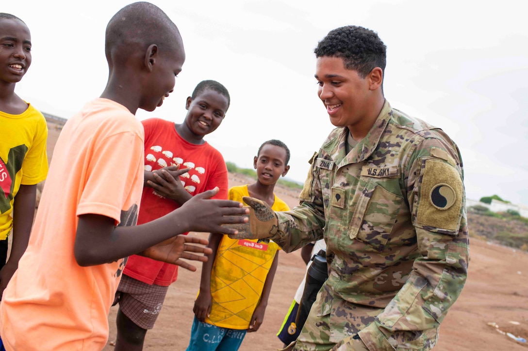 A soldier plays games with a child as other children surround.