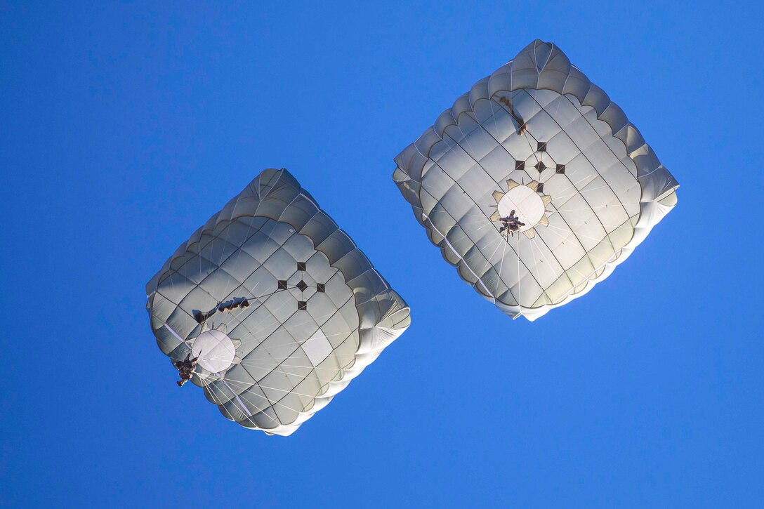 Two soldiers descend in the sky wearing parachutes.