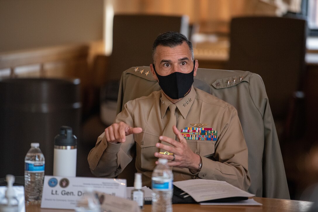A man in a uniform is seated at a table and is speaking to a group at the table.