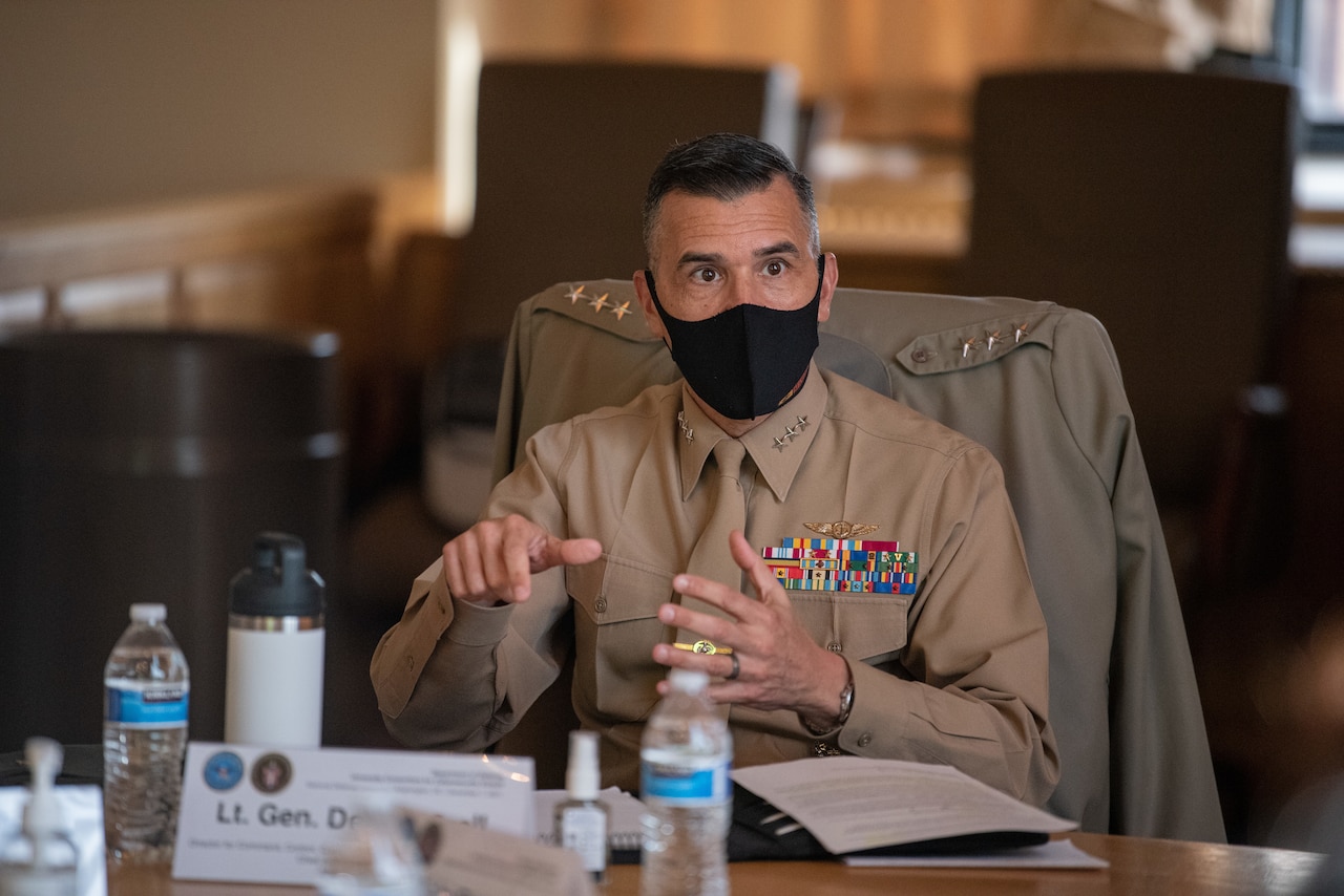 A man in a uniform is seated at a table and is speaking to a group at the table.
