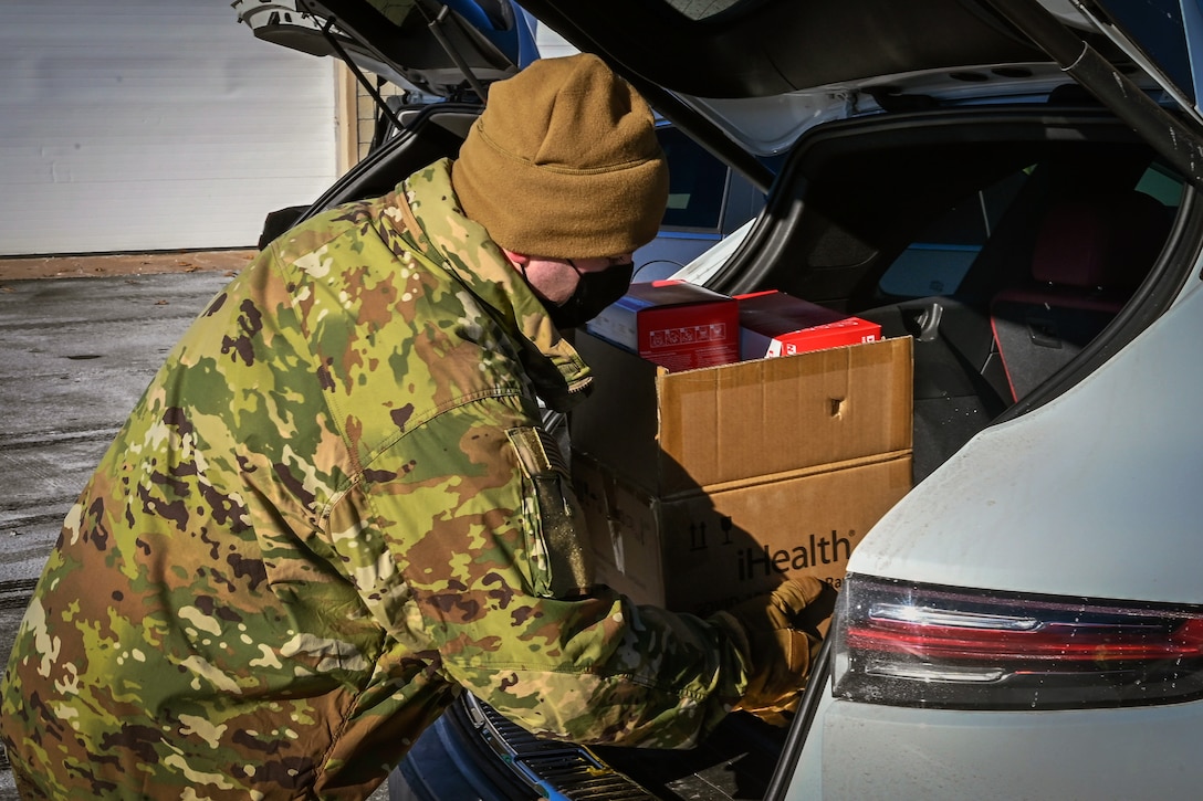 An airman puts a box into the trunk of a vehicle.