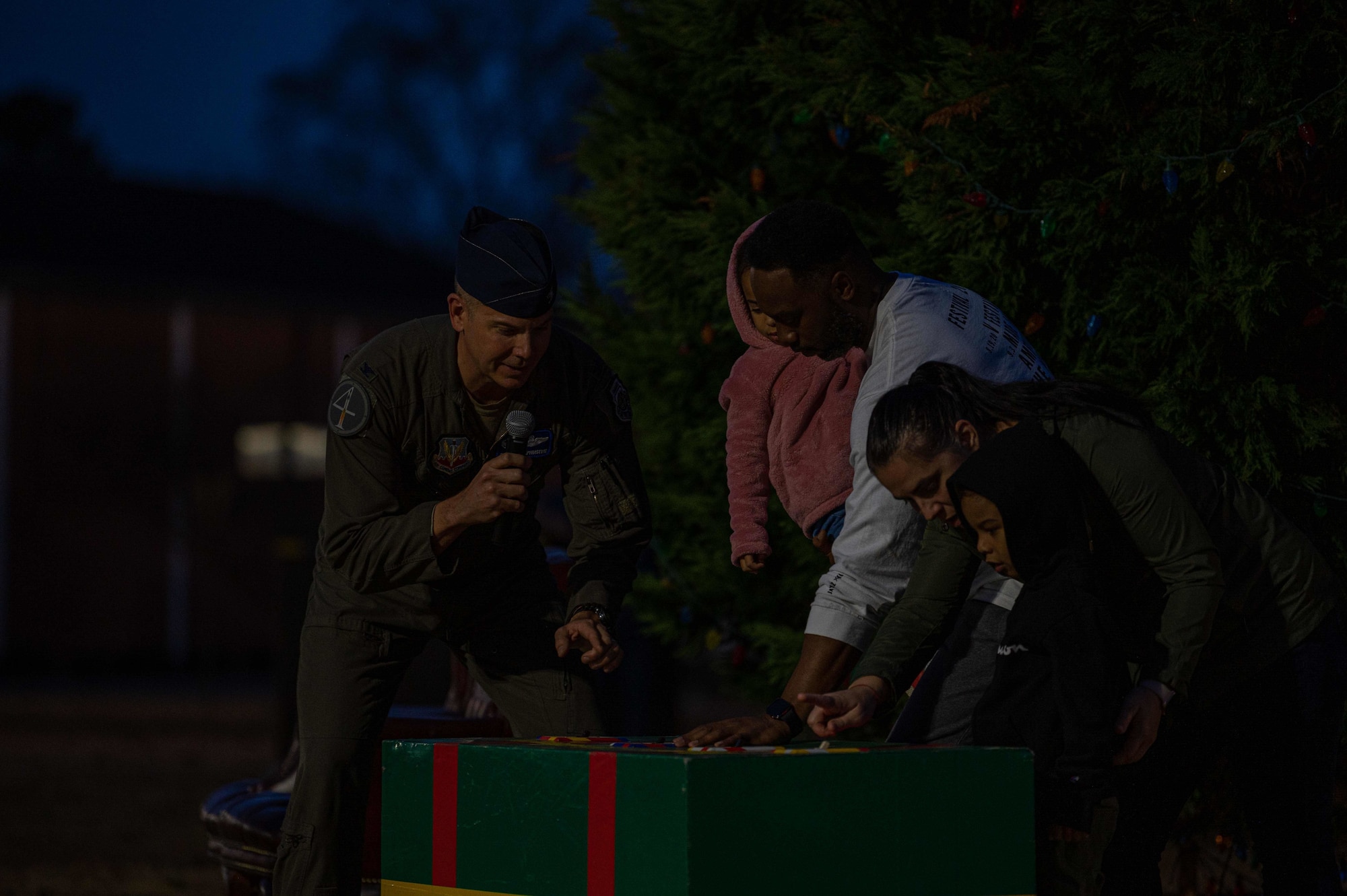 Col. Kurt Helphinstein, 4th Fighter Wing commander, switches on the lights of a holiday tree with a family at Seymour Johnson Air Force Base, North Carolina, Dec. 8, 2021. Members of the Seymour Johnson AFB Youth Center sang Christmas carols at the tree lighting event. (U.S. Air Force photo by Airman 1st Class Sabrina Fuller)