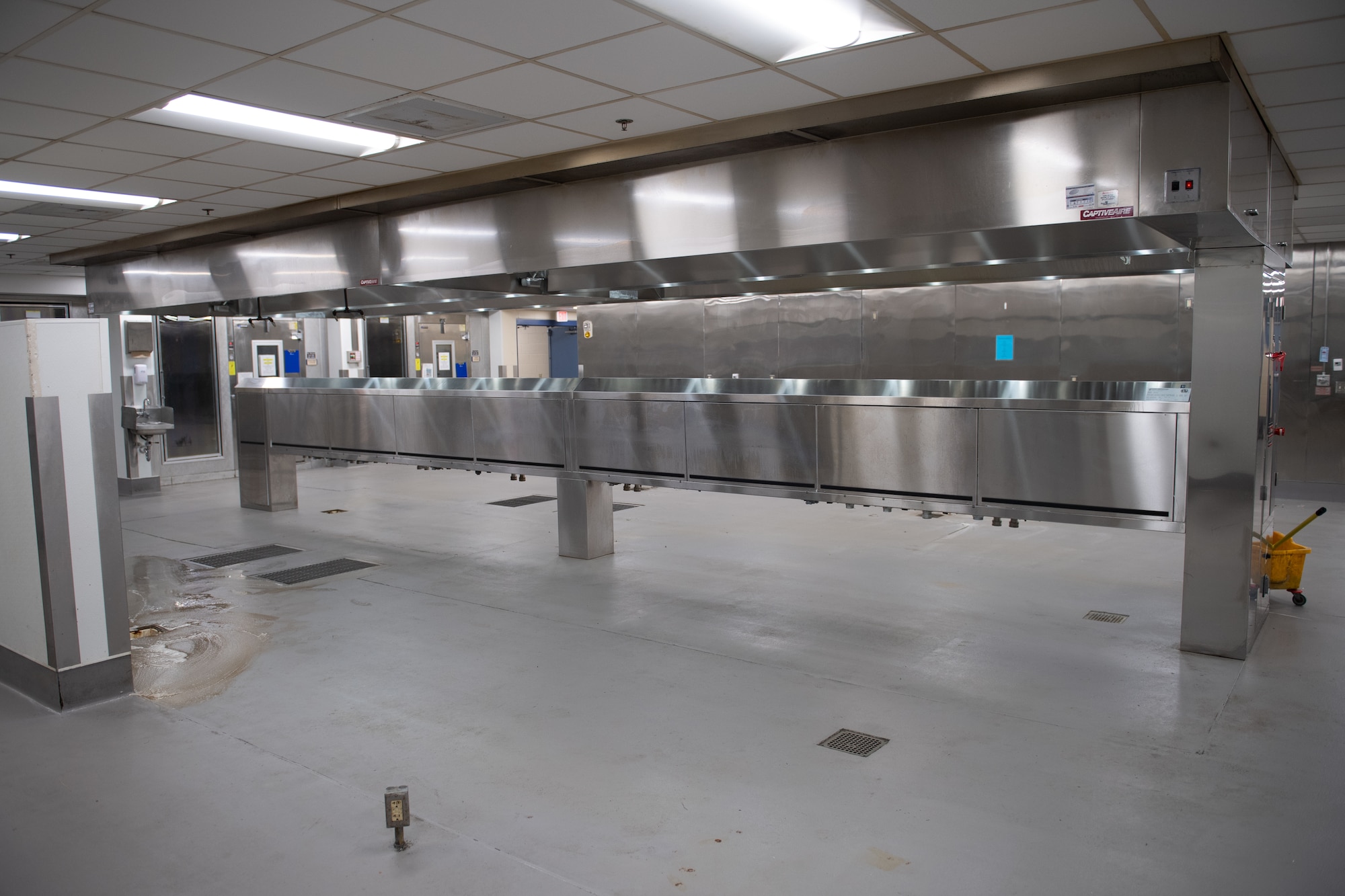 A photo of an empty kitchen with steel appliances and grey floors.