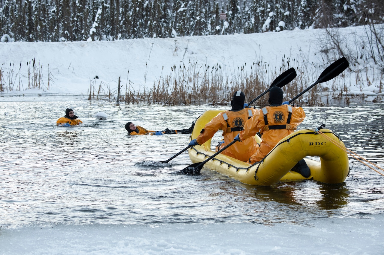 Airmen row a raft toward two men in the water.