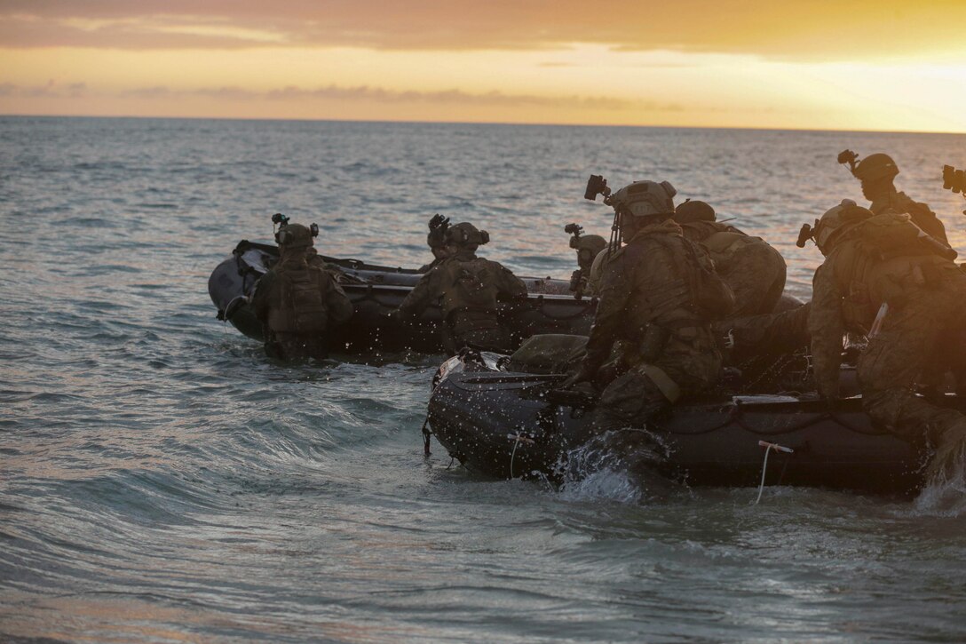 Marines ride in rubber boats under a sunlit sky.