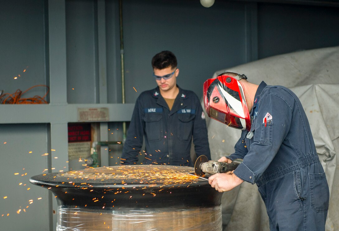 Sparks fly as a sailor uses a grinder wheel aboard a ship at sea.